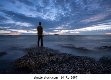 Tranquil Stony Bay With A Rear Of Man After Sunset. Slow Shutter Speed For Smooth Water Level And Dreamy Effect.