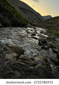 A tranquil stream flows over rocks through grassy terrain under a twilight mountain sky—capturing nature’s soft motion, rugged textures, and peaceful atmosphere as the New Year approaches.