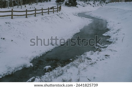 A tranquil stream meanders through a pristine winter landscape of snow-covered fields