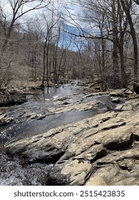 A tranquil stream winds through Shenandoah National Park, its clear water gently flowing over smooth stones. Surrounded by lush greenery, the peaceful scene captures the beauty of nature.