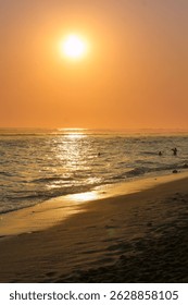 A tranquil sunset over a beach, casting warm hues on the water. People enjoy a peaceful swim, embracing the serene atmosphere.