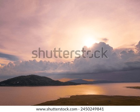 A Tranquil Sunset over a Lake with a Small Island. The sky is ablaze with hues of orange, pink, and purple, as the sun dips below the horizon. Chonlasit Dam, Saraburi, Thailand