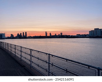 A tranquil sunset over the Thames River in London, UK, silhouetted against the dramatic, cloud-filled sky. The warm, golden tones and reflective water create a peaceful and atmospheric scene. - Powered by Shutterstock