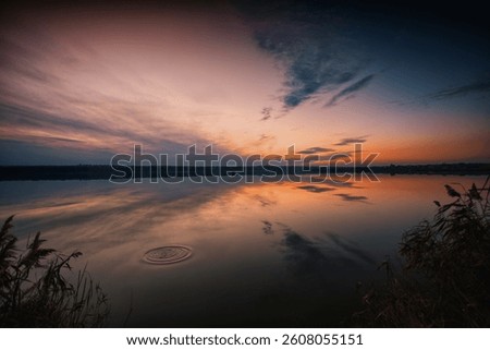 Tranquil sunset reflected on still lake waters. Warm orange tones and soft clouds create a peaceful natural scene