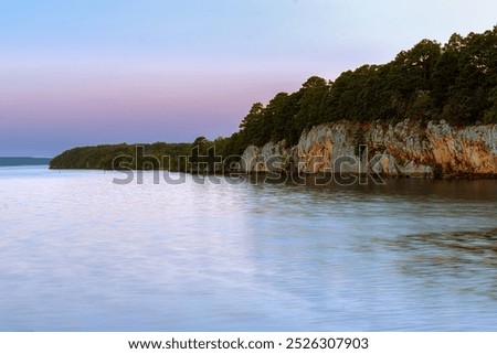 A tranquil sunset scene at Atoka Oklahoma Park featuring calm waters reflecting the soft pastel hues of the evening sky. 