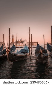 Tranquil sunset scene of gondolas reflected in calm waters. No people or birds present. Part of a collection showcasing popular places in Venice, Italy.