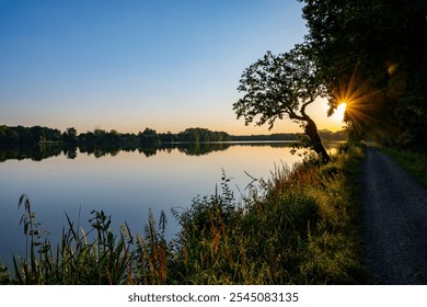 The tranquil Trebonsko Pond System in South Bohemia glows as the sun sets, reflecting golden light on calm waters flanked by lush greenery and a peaceful pathway. - Powered by Shutterstock