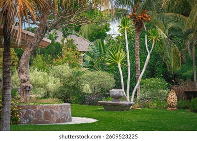 Tranquil tropical garden in Bali with ornamental plants, coconut palm trees, stone fountain and decorative sculpture. A lush, vibrant setting ideal for relaxation and luxury travel themes.