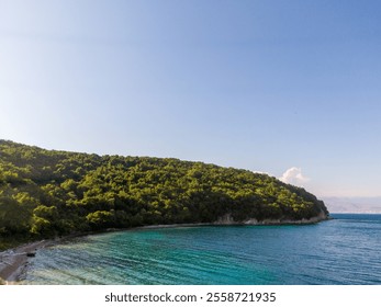 Tranquil turquoise bay with lush green hillside under clear blue sky. - Powered by Shutterstock