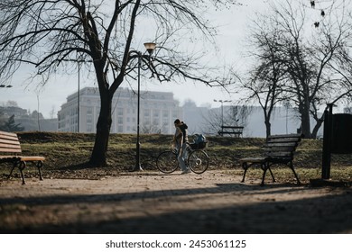 A tranquil urban park setting depicting a cyclist pausing to enjoy the morning sun, with benches and leafless trees enhancing the peaceful ambiance. - Powered by Shutterstock