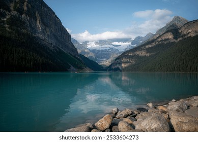 A tranquil view of Lake Louise with turquoise waters, rocky shoreline, and majestic mountains in Banff National Park, Canada. - Powered by Shutterstock