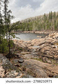 A tranquil view of a lakeside surrounded by rocky terrain and lush trees under a cloudy sky.