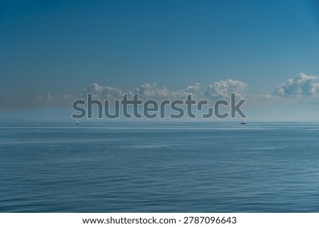 A tranquil view over Lake Constance (Bodensee) in Switzerland, showing a smooth blue surface under a bright sky dotted with white clouds, with sailboats visible in the distance.