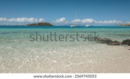 Tranquil waves lapping against pristine beach in Bora Bora, with sailboats and luxurious overwater bungalows in background. Wild nature paradise. Popular tourist destination, exotic summer vacation