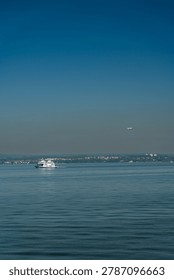 A tranquil and wide-angle view capturing a passenger ferry cruising across the vast expanse of Lake Constance (Bodensee) in Switzerland, bordered by distant shores under a clear, deep blue sky. The scene conveys a sense of peaceful travel and regional beauty.