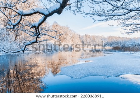 A tranquil winter scene of a frozen river reflecting the icy blue sky, surrounded by snow-covered trees in Mölndal, Sweden.