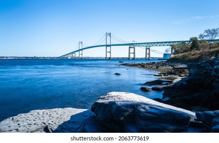 Tranquil wintry seascape with the view of Claiborne Pell Newport Bridge and rocky beach on Route 138 in Rhode Island. Smooth water flows under the bridge, long exposure photography.