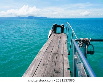 A tranquil wooden pier stretches into the vibrant turquoise ocean, offering a stunning view of distant mountains under a clear blue sky. - Powered by Shutterstock