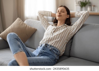 Tranquil young woman enjoying peaceful moment, reclining with hands behind head on soft sofa, embodying relaxation and comfort at home, free space - Powered by Shutterstock