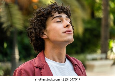 Tranquility. Portrait of a happy caucasian curly man relaxing with closed eyes while standing at the street at the park. Stock photo  - Powered by Shutterstock