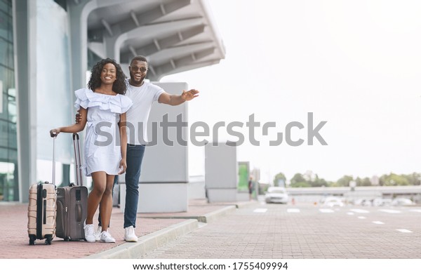 Transfer From Airport. Young African\
Couple Catching Taxi On Parking Near Terminal, Copy\
Space