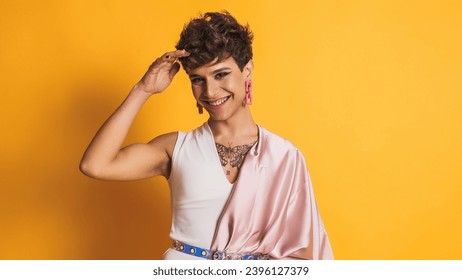 Transgender man with pink clothes and make up smiling at the camera on yellow - Powered by Shutterstock