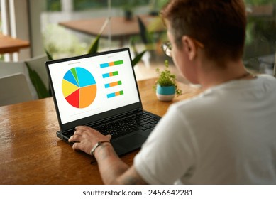 Transgender office worker analyzes data charts on laptop screen in bright workspace. Pro with tattoo interacts with business analytics report. Inclusive workplace, modern employee engaged in market. - Powered by Shutterstock - Get 15% off with code: PIKWIZARD15