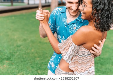 A transgender woman and a man dance together in a park. The man is wearing a blue shirt with flowers. The woman is wearing a pink and white shirt. They are both smiling and having fun. - Powered by Shutterstock