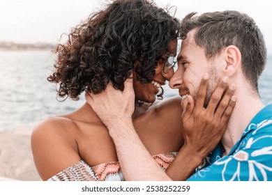 A transgender woman and a man embrace and caress each other's faces in front of the sea. The woman has curly hair and the man wears glasses. Both are smiling and seem to enjoy each other's company. - Powered by Shutterstock