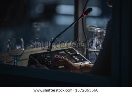 Translator or translation booth at a conference. Hand of a person for simultaneous translating is seen working in a booth. Glass of water next to a translator.