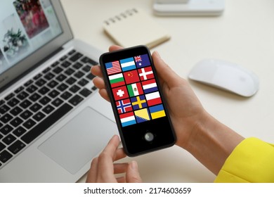 Translator using smartphone with images of different flags on screen at table, closeup