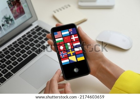 Translator using smartphone with images of different flags on screen at table, closeup