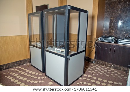 translators cubicle . interpreting - Microphone and switchboard in an simultaneous interpreter booth . Soft focus of wireless Conference microphones and notebook in a meeting room.