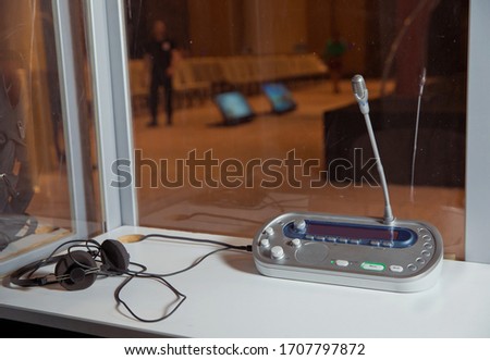 translators cubicle . interpreting - Microphone and switchboard in an simultaneous interpreter booth . Soft focus of wireless Conference microphones and notebook in a meeting room.