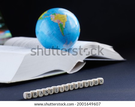 Transliteration inscription next to globe and open book. Concept of educational work on translation and transliteration of texts. Selective focusing. Macro