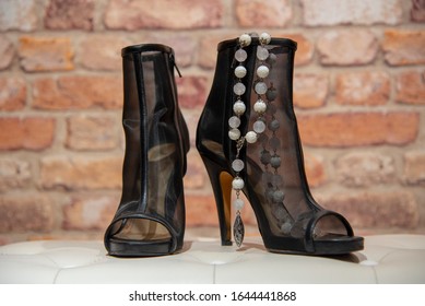 Translucent Black Summer Women's Stiletto Boots And White Stone Beads On A White Leather Banquette Against A Brick Wall. Women's Glamorous Accessories.