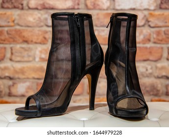 Translucent Black Summer Women's Stiletto Boots On A White Leather Banquette Against A Brick Wall. Women's Fashion Shoes.