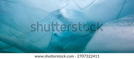 Translucent ice layers and formations appear above, with a turquoise hue, on the surface of frozen Lake Baikal. Sunlight filters through in winter.