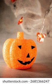 Translucent orange jack-o’-lantern with a textured bubble surface sits on artificial snow. Neutral gray background enhances its warm glow, blending Halloween charm with a hint of winter magic.