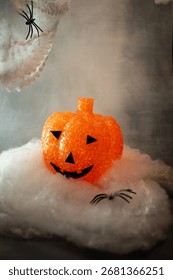 Translucent orange jack-o’-lantern with a textured bubble surface sits on artificial snow. Neutral gray background enhances its warm glow, blending Halloween charm with a hint of winter magic.