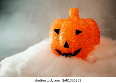 Translucent orange jack-o’-lantern with a textured bubble surface sits on artificial snow. Neutral gray background enhances its warm glow, blending Halloween charm with a hint of winter magic.