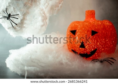 Translucent orange jack-o’-lantern with a textured bubble surface sits on artificial snow. Neutral gray background enhances its warm glow, blending Halloween charm with a hint of winter magic.
