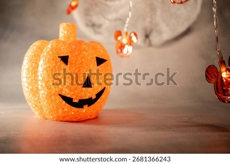 Translucent orange jack-o’-lantern with a textured bubble surface sits on artificial snow. Neutral gray background enhances its warm glow, blending Halloween charm with a hint of winter magic.