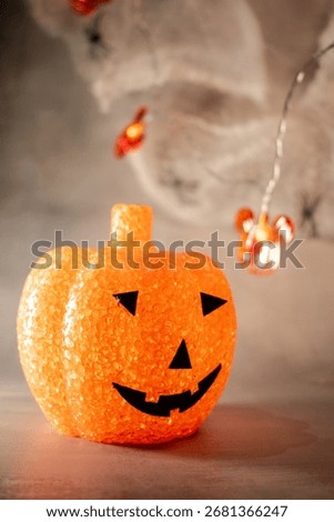 Translucent orange jack-o’-lantern with a textured bubble surface sits on artificial snow. Neutral gray background enhances its warm glow, blending Halloween charm with a hint of winter magic.