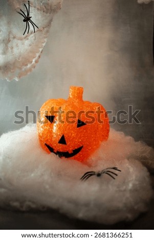 Translucent orange jack-o’-lantern with a textured bubble surface sits on artificial snow. Neutral gray background enhances its warm glow, blending Halloween charm with a hint of winter magic.