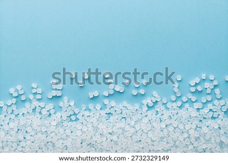 Translucent plastic pellets scatter on blue background with wide copy space, raw polymer feedstock for medical injection molding.