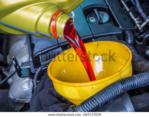 Transmission oil fill up in a car engine with yellow\
cone spire shape container\
.