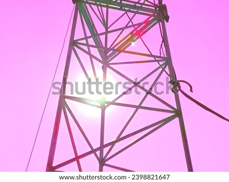 A transmission tower with the sun shining through it. The tower is metal and the sky is blue.