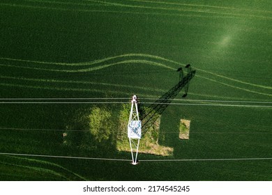 Transmission Tower Supporting Overhead Power Line Through Cultivated Crops Field, Aerial View From Drone Pov Directly Above