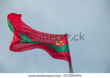 Transnistrian flag, featuring the Soviet hammer and sickle and red star, proudly flying against a clear sky, representing national identity and the unrecognized state's ties to its communist past